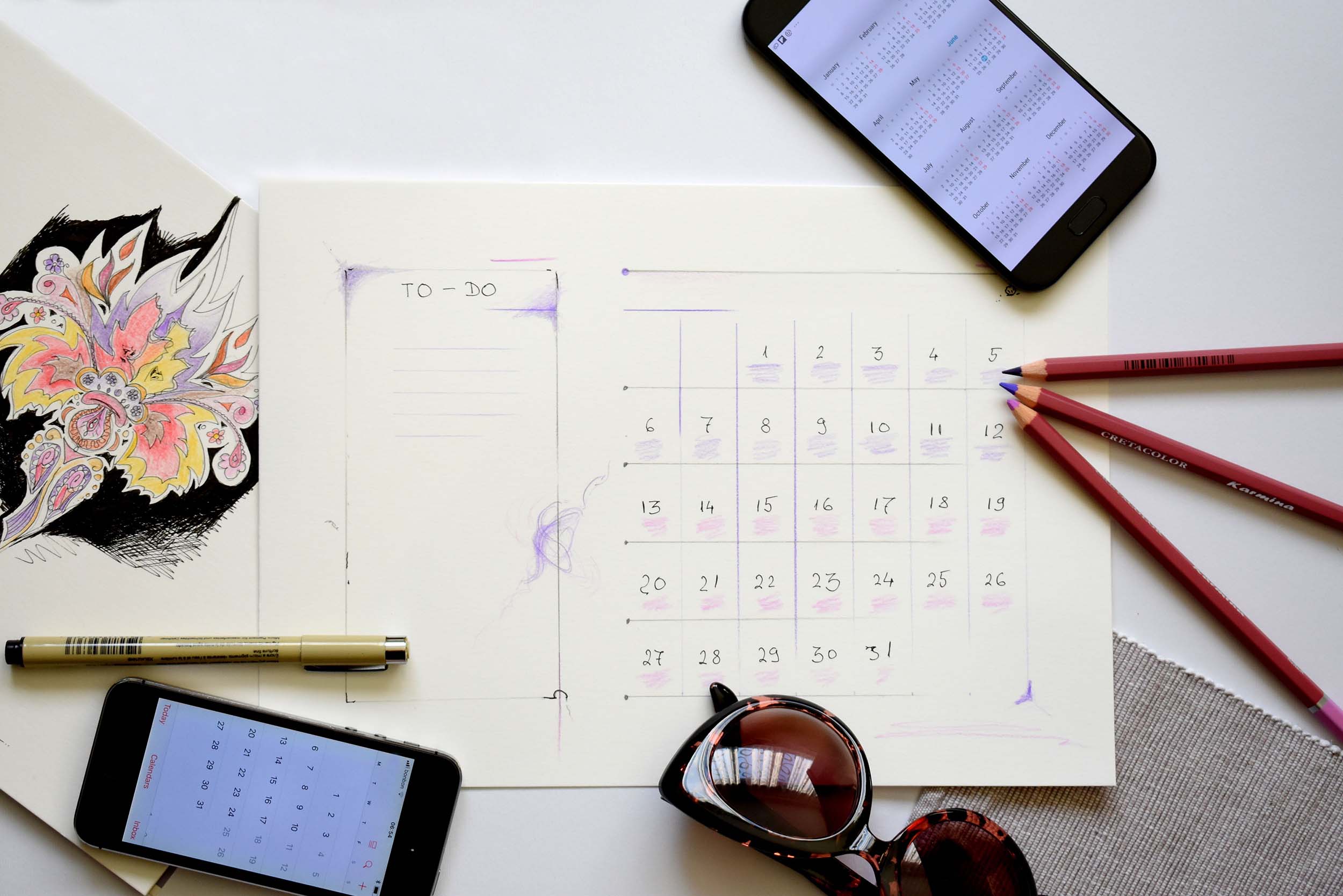 Calendar, pencils, and phones laid out on a desk
