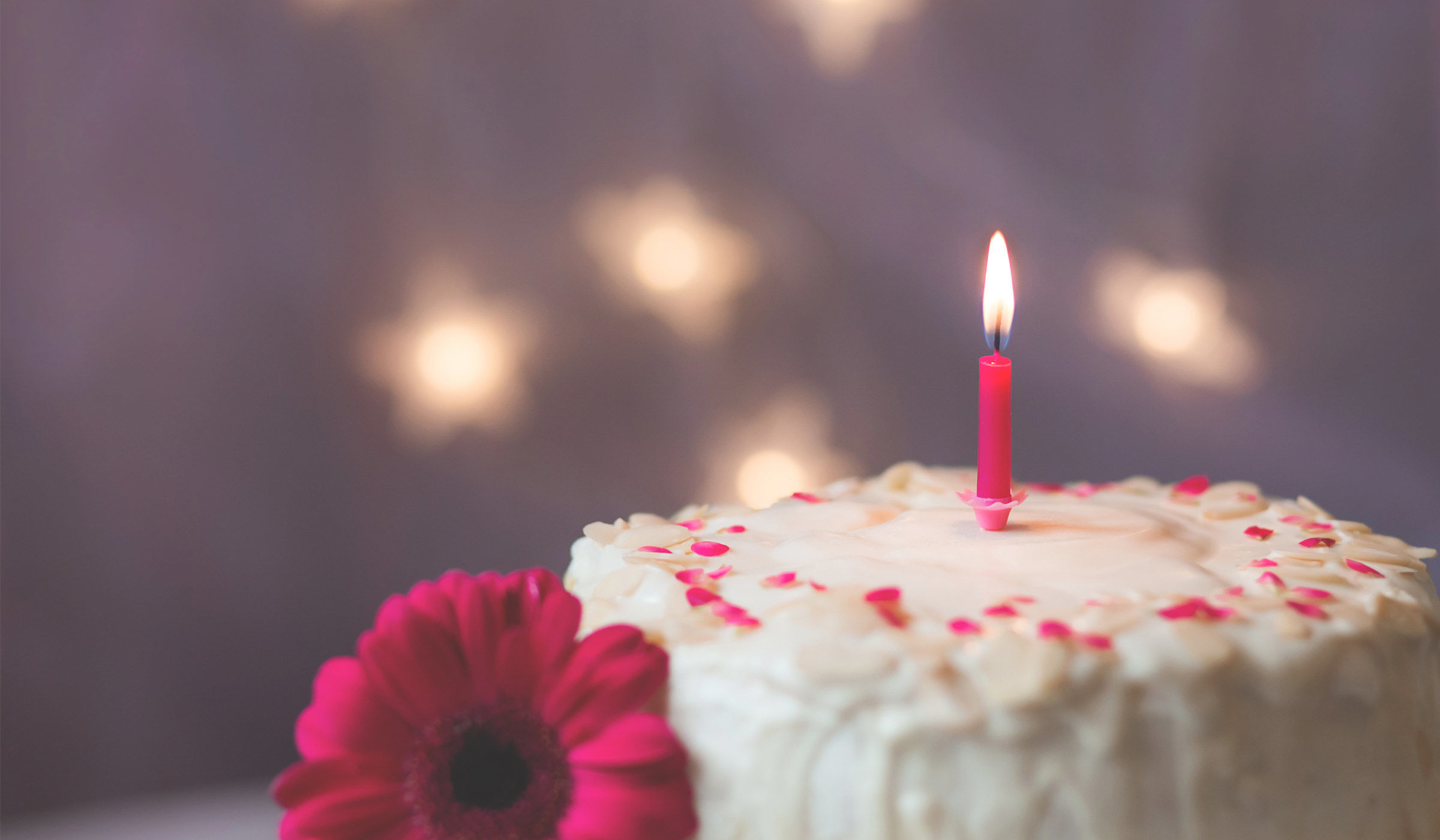 White frosted cake with pink flower and pink candle on top